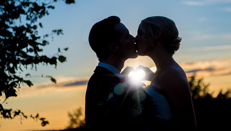 Das Brautpaar küsst sich während des Sonnenuntergangs. Ihre Hände umkreisen dabei die Sonne.