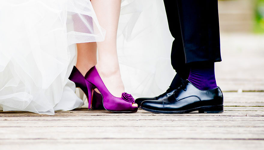 Ein Brautpaar stellt die Zehenspitzen zueinander und sie hebe ihre Kleidung damit wir ihre Schuhe erkennen können. 