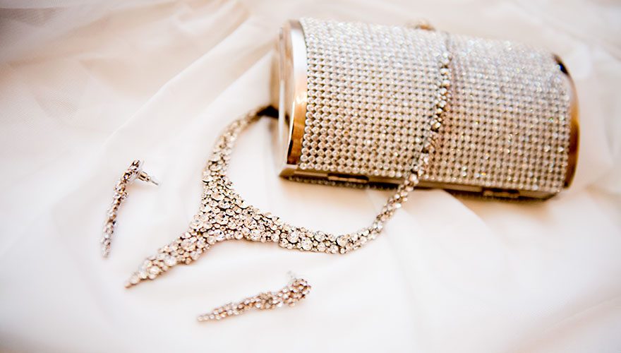 Auf einem weissen Tuch liegt eine silberne Handtasche mit einer Glasperlenoberfläche. Darüber liegt eine silberne Modeschmuck-Kette mit Glassteinen.