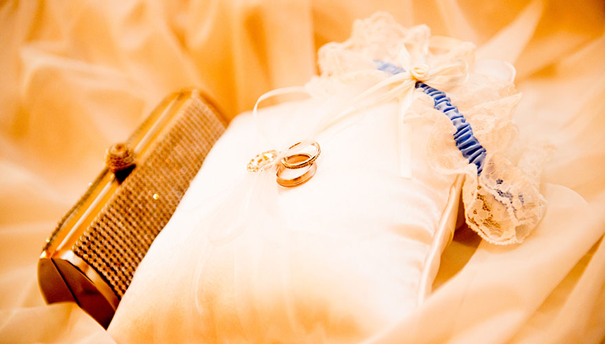 2 Eheringe auf einem Ringpolster und daneben sind das Strumpfband und die Handtasche der Braut.