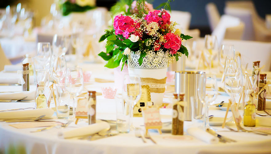 Ein Tisch auf einer Hochzeitstafel, fertig dekoriert. man erkennt Blumen, Gastgeschenke, Gläser, Servietten und Namenskarten mit Ständer welche wie Mal-Staffelein aussehen.