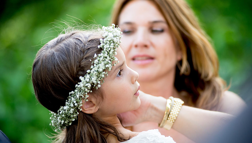 Eine Mutter setzt Ihrer Tochter einen Blumenkranz auf. Der Blumenkranz mit weissen Blüten passen stimmig zu den langen Haaren.