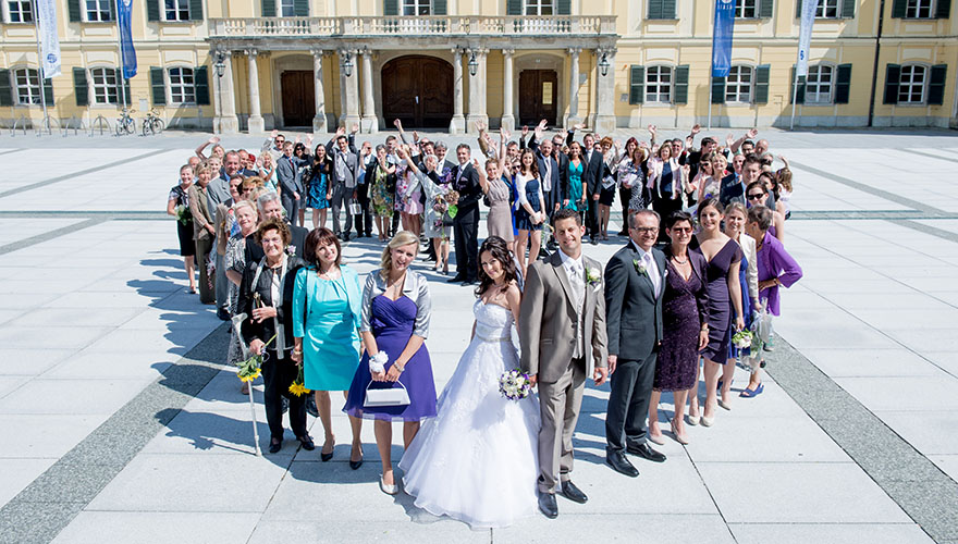 Eine Hochzeitsgesellschaft am Kirchenplatz in Laxenburg hat sich in Herzform aufgestellt und präsentiert sich so dem Fotografen.