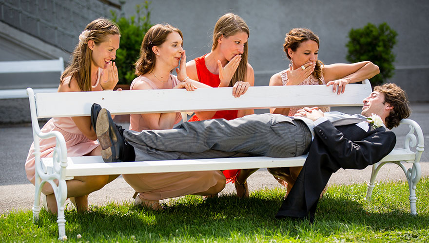 Ein Bräutigam liegt auf einer Parkbank. Hinter der Parkpank sind vier Brautjungfrauen und veräppeln den Bräutigam mit anscheinend erstaunten Gesichichtern.