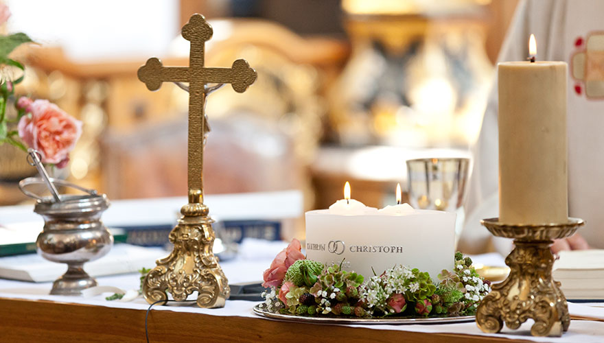 Auf einem Kirchenaltar steht eine Hochzeitskerze. Sie ist bereits angezündet. Auf der Kerze stehen die Namen des Brautpaares: Kathrin und Christoph.