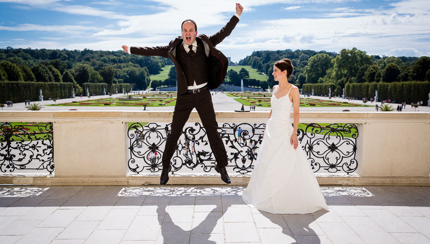 Die grosse Terasse des Schloss Schönbrunn in Wien ist Kulisse. Ein Bräutigam springt hoch in die Luft. Seine Arme sind weit ausgestreckt und er schreit. Seine Braut steht ganz gelassen daneben und betrachtet sein Treiben. Im Hintergrund erkennt man den P