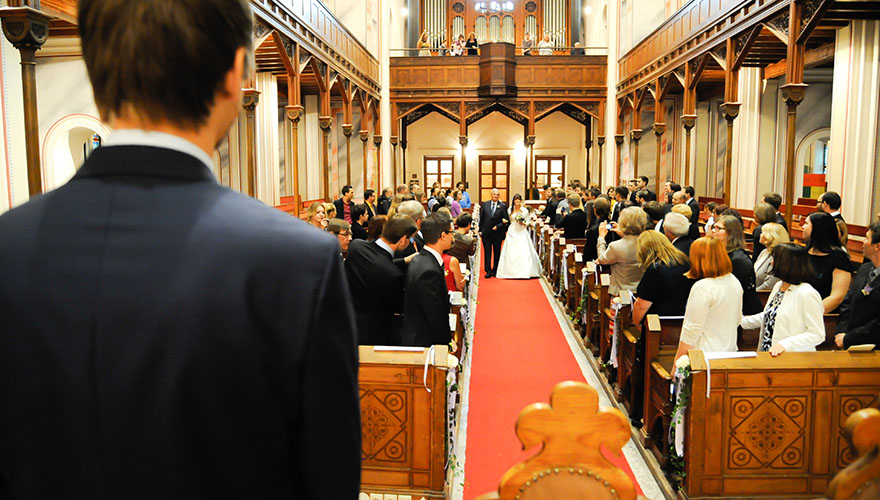 In einer Kirche steht der Bräutigam und die Brau kommt mit ihren Vater durch den Mittelgang.