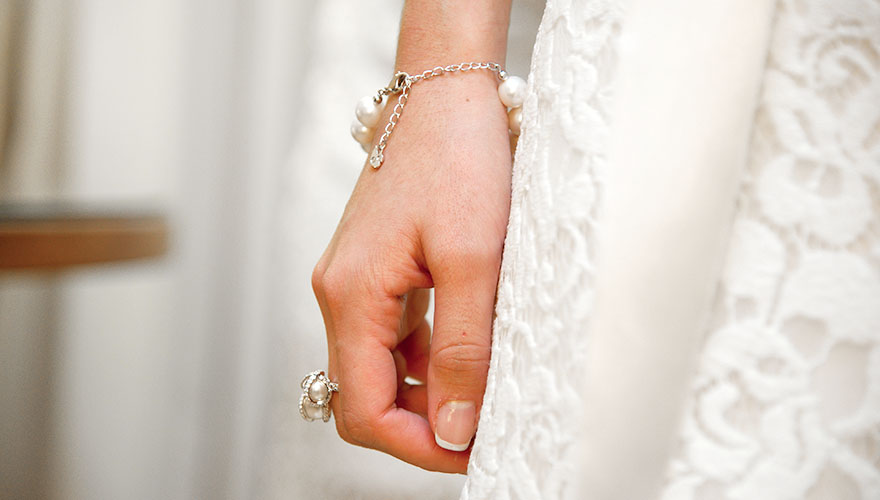 Eine Braut lässt Ihre Hand locker hängen und man erkennt den Schmuck der reichlich mit Perlen bestückt ist.