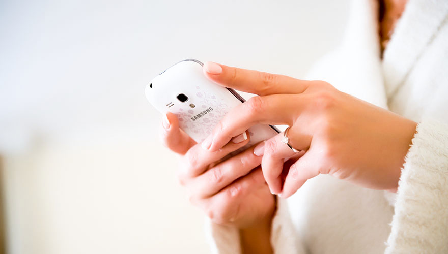 Eine Braut betätigt Ihr Mobiltelefon. Auf Ihrer Hand erkennt man sehr deutlich ihren Verlobungsring mit einem funkelden Stein.