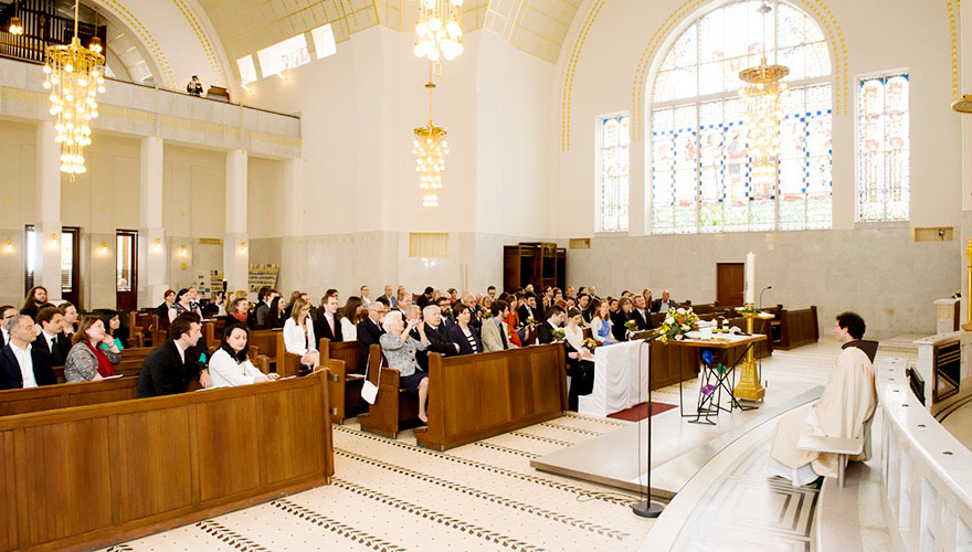 Eine Hochzeit findet in der Kirche von Otto Wagner auf der Baumgartner Höhe statt. Die Gäste lauschen einem Konzert eines Musikers welcher am Balkon steht.